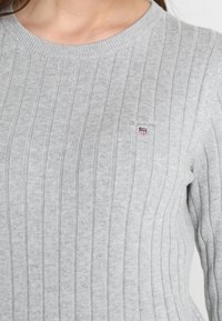 Maglione grigio a coste realizzato in un tessuto morbido, con collo rotondo e un logo ricamato nella parte sinistra del petto.