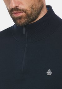 Marineblauer Reißverschluss-Pullover mit hohem Kragen, geripptem Textur und kleinem weißen Pinguin-Logo. Verfügt über einen kurzen schwarzen Reißverschluss.
