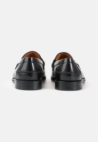 Svarta läderloafers med en slät yta, rund tå och sömnad detaljer. Låg klack i staplad design och inredning är brun.