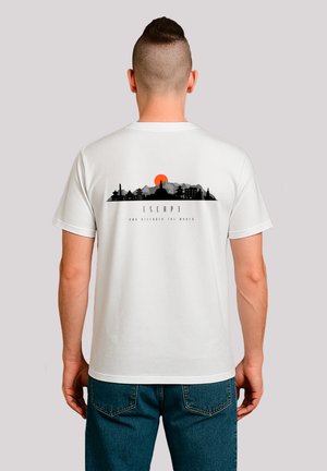 Mann trägt ein weißes T-Shirt mit einem schwarzen und orangenen Berg- und Stadtbildgrafik sowie dem Text "FLIEH UND ENTDECKE DIE WELT" auf dem Rücken.
