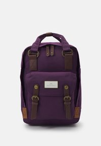 Purple canvas backpack with brown leather accents, dual top handles, front pocket, and buckle closures. Features a logo patch on front.