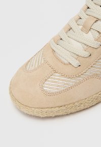 Sneaker en suède beige avec des accents en maille tissée et des lacets écrus, dotée d'une semelle en corde de jute. Surface texturée, design décontracté.