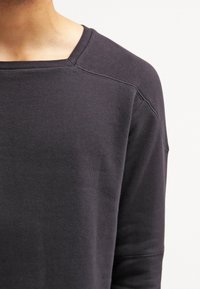 Sudadera negra de manga larga con un escote ancho y un tejido suave y texturizado. Presenta mangas raglán y detalles de costura sutiles.