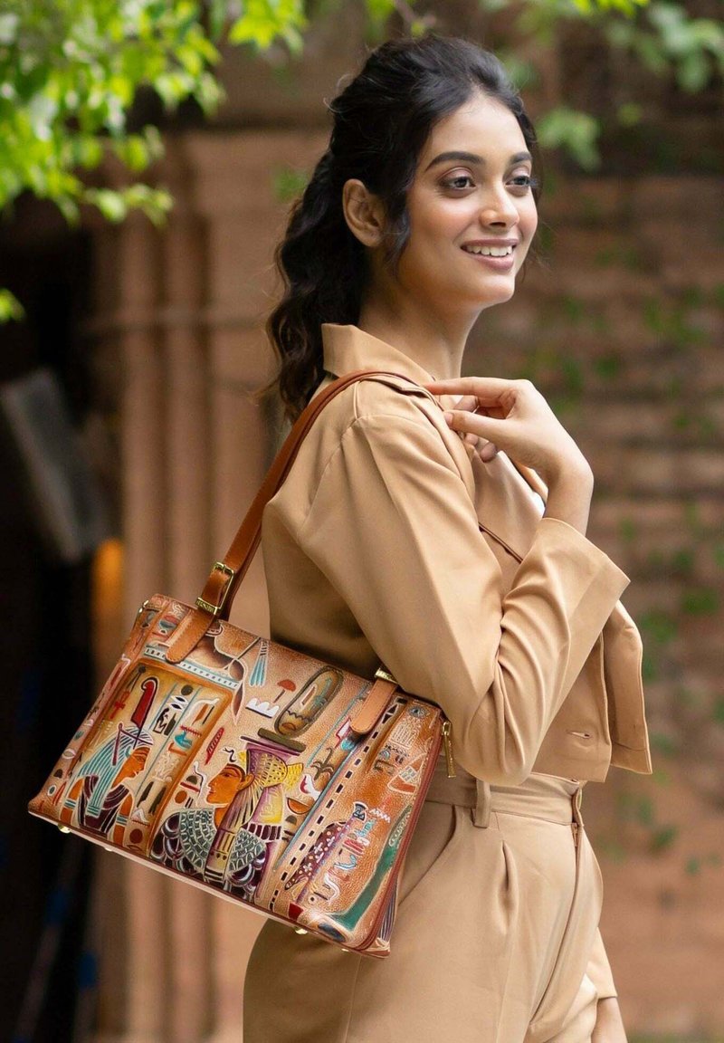 Tan leren handtas met gedetailleerd Egyptisch patroon in levendige kleuren; voorzien van schouderriem en gouden hardwareaccenten.