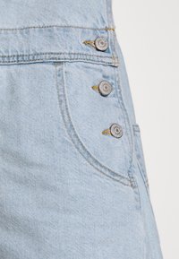 Falda de mezclilla azul clara con tres botones metálicos en la cintura, con costuras amarillas y una textura suave.