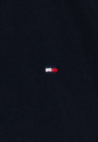 Small rectangular logo with white, red, and blue horizontal stripes centered on a black fabric background.