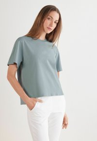 Krátký rukáv, kulatý výstřih, top z měkké, tlumené tyrkysové látky s hladkým povrchem, spárovaný s bílými kalhotami a volným střihem.