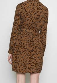 Hnědé šaty chemise s černým tečkovaným vzorem, s dlouhými rukávy a páskem na zavazování v pase. Měkká látka s volnějším střihem.