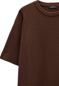 Brązowy sweter z dzianiny o okrągłym dekolcie, krótkich rękawach i ribbowanych wykończeniach przy dekolcie i rękawach. Miękka tekstura.