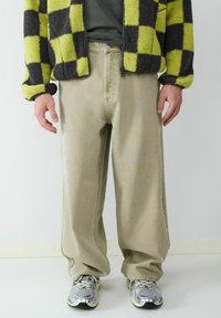 Beige wijde broek gecombineerd met een zwart en limoen groen geruite fleece jasje en zilveren sportsneakers. Zachte textuur en relaxte pasvorm.