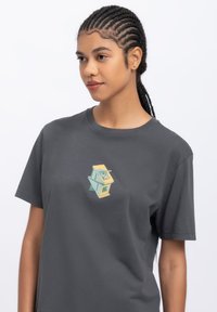 Grijze katoenen t-shirt met een kleurrijk geometrisch ontwerp op de borst. Korte mouwen met een ontspannen pasvorm en zachte textuur.