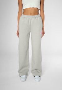 Light gray sweatpants with a loose fit, elastic waistband, and subtle pink logo detailing on the left thigh. Pairing with white sneakers.