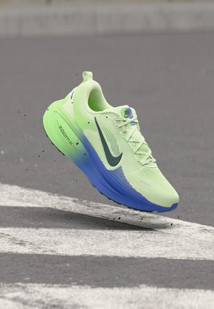 Neongrøn og blå Nike løbesko med ZoomX-sål, let over asfalt med små jordpartikler omkring.