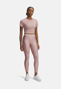 Rosa sportlicher Crop-Top und hochgeschnittene Leggings mit glatter Textur. Die Leggings verfügen über Mesh-Details und eine taillierte Passform. Weiße Sneakers runden den Look ab.