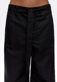 Black linen trousers with a wide-leg design, featuring a tied waist belt and subtle texture. No visible patterns or accents.