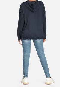 Marinblå huvtröja med en lös passform, med en texturerad nederkant. Kombinerad med ljusblå skinny jeans och vita sneakers.