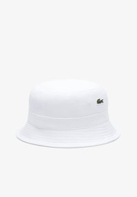 Weißer Bucket Hut aus Baumwolle; hat eine abgerundete Oberseite, einen breiten Rand und ein kleines grünes Krokodil-Logo, das an der Seite gestickt ist.