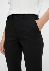 Svarta skräddarsydda byxor med slim fit, slät yta, bältesöglor och sidfickor. Tyget verkar vara strukturerat och formellt.