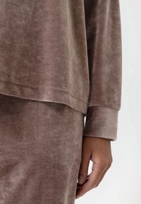 Bruine velours lange mouwen top met een relaxte pasvorm, ronde halslijn en manchet mouwen. Zachte textuur met subtiele glans en gladde naden.