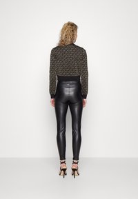 Maglione nero corto con un motivo texture, abbinato a leggings neri lucidi a vita alta e tacchi neri con cinturini.