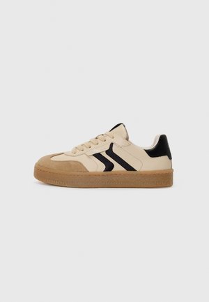 Beige sneakers with black accents, suede and leather materials, low-top design, round toe, textured tan rubber sole, and lacing system.