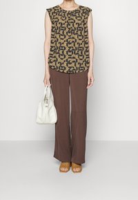 Korte mouwen patroon top in beige en zwart, bruine wijde broek, geweven tan sandals, met een witte handtas. Eenvoudige, geometrische ontwerpen.