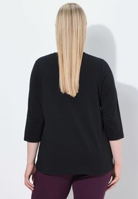 Černý top s tříčtvrtečním rukávem a kulatým výstřihem, doplněný fialovými legínami. Hladká tkanina a jednoduchý design, bez viditelných vzorů nebo akcentů.