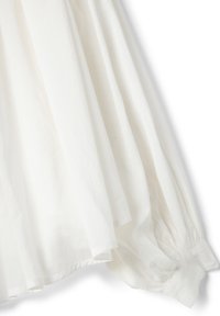 Blusa blanca de manga larga con puños fruncidos y detalle de tela fluida sobre un fondo liso.