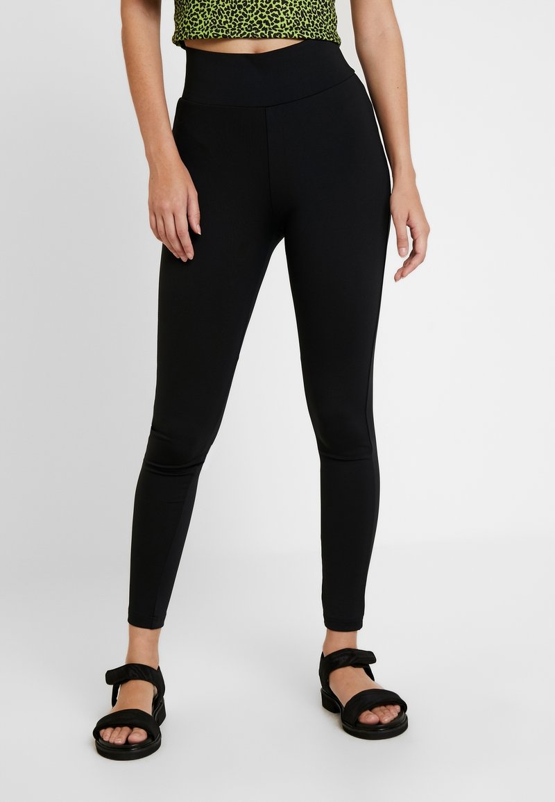 Leggings noires taille haute avec une texture lisse et une coupe ajustée, associés à des sandales noires avec une large bride et un bout ouvert.