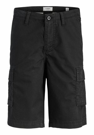 Dreng stående med den ene hånd i lommen, iført en hvid t-shirt, sorte cargoshorts, stribede sokker og sorte-hvide sneakers mod en ensfarvet baggrund.