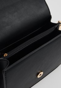 Borsa a mano in pelle nera con chiusura dorata, dotata di tasca interna con zip e texture liscia. Design strutturato con forma rettangolare.