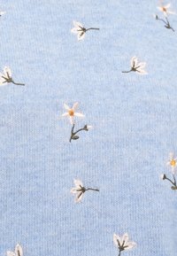 Ανοιχτό μπλε ύφασμα με μικρά λευκά κεντημένα λουλούδια που έχουν κίτρινα κέντρα και πράσινα κοτσάνια, διασκορπισμένα σε όλη την επιφάνεια.