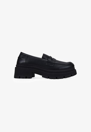 Mocasines de cuero negro con suela de goma gruesa, que presentan un toe redondo y un detalle de correa horizontal en el empeine. Costura lateral texturizada.
