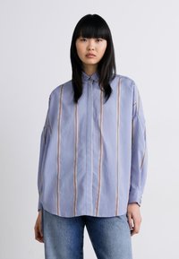Light blue oversized shirt featuring vertical stripes in shades of red and cream; button-up design with a classic collar and dropped shoulders.