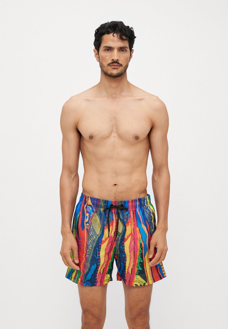 Shorts de bain colorés fabriqués en tissu léger, avec des motifs vibrants rouge, bleu, jaune et vert, dotés d'une taille élastique et d'un cordon de serrage.