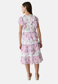 Blumengemustertes Kleid in hellrosa, mit Rüschendetails an den Ärmeln, geschichteter Gestaltung und Spitzenakzenten. Weicher, leichter Stoff.