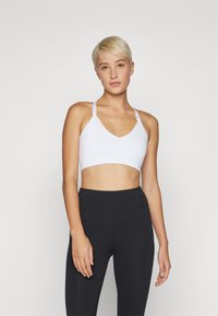 Hvit sports-bh med V-hals, justerbare stropper og en glatt, elastisk bånd. Brukt med svarte høyt liv leggings. Minimalistisk design.