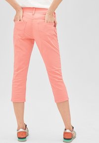 Pantalons cropped pêche en coton, dotés de deux poches arrière, de coutures plates et d'une coupe droite. Portés avec des baskets multicolores.