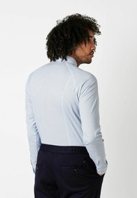 Hellblaues Hemd mit kleinen dunkelblauen Pollenkreisen, Slim Fit, lange Ärmel und Kragen, kombiniert mit dunkelblauen Hosen.