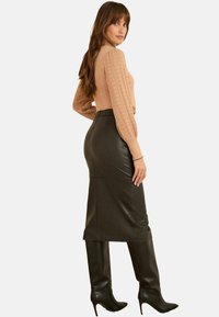 Beige Strickpullover mit strukturierten Ballonärmeln, kombiniert mit einem figurbetonten schwarzen Lederrock und knielangen, schwarzen, spitzen Stiefeln.
