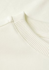 Sweatshirt beige clair avec un col rond côtelé et une texture douce, en tissu lisse avec des détails de couture visibles.