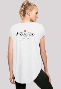 Witte t-shirt met korte mouwen en een gebogen zoom, met een zwarte bergafbeelding, groene bomen en een rode zon met de tekst "ONTGLIP EN ONTDEK DE WERELD."