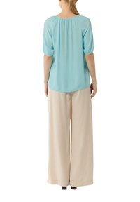 Light blue blouse with a rounded neckline and gathered back, paired with beige wide-leg pants, both made of soft, lightweight fabric.