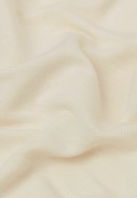 Lys cremefarvet stof med en glat, blød tekstur; vævet mønster synligt med en subtil glans skabt af lysrefleksioner.