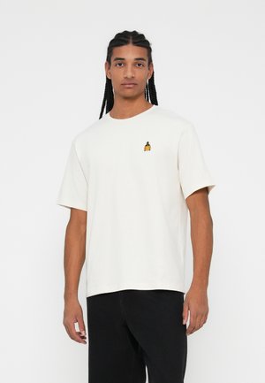 Tricou din bumbac crem, cu un mic design brodat galben pe piept, cu mâneci scurte și o croială lejeră. Pantaloni negri.