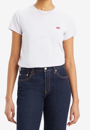 Biały T-shirt z krótkim rękawem z czerwonym logo Levi's na lewej piersi, zestawiony z ciemnoniebieskimi wysokim stanem jeansami z miedzianymi elementami.