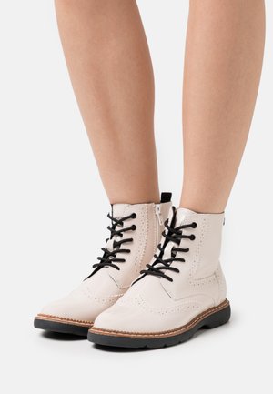Short lace-up ankle boots in glossy light pink leather with black laces, brogue detailing, and a rubber sole for traction.