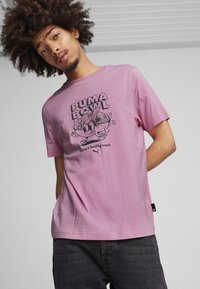 Rosa Baumwoll-T-Shirt mit einem Grafikdruck, der den Text "PUMA BOWL" und Cartoon-Designs zeigt. Kurzarm mit lockerer Passform.