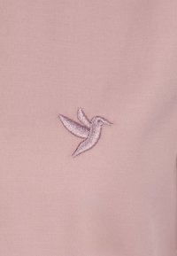 Tessuto rosa chiaro con un piccolo colibrì ricamato in filo lavanda, che dettaglia ali e forma del corpo delicati.