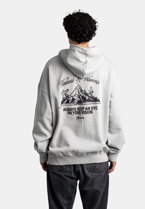 Light grey hoodie with a front kangaroo pocket and a drawstring hood. Back features black graphic text and mountain design. Cotton blend material.